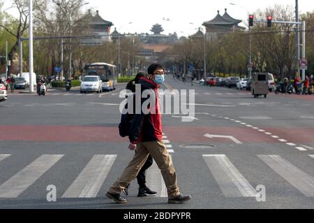 Peking, China. April 2020. Chinesen, die Schutzmasken tragen, gehen am Donnerstag, den 9. April 2020 durch eine Kreuzung im Zentrum Pekings. Chinas Hauptstadt bremst die Rückkehr zu einem "normalen" Leben von drakonischen Sicherheitsmaßnahmen aufgrund des Covid-19-Ausbruchs, da die Regierung langsam einige Einschränkungen für Reisen und soziale Interaktionen aufhebt. Foto von Stephen Shaver/UPI Credit: UPI/Alamy Live News Stockfoto