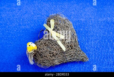 Ringe an ein Herz aus Ästen mit einem gelben Vogel auf blauem Hintergrund gebunden. Stockfoto
