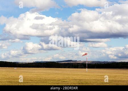 Rot-weiße Windsack auf leerem grasbewachsenen Flugplatz, dramatische Wolken im Hintergrund, windige Wettervorhersage und Flugverkehrskonzept Stockfoto