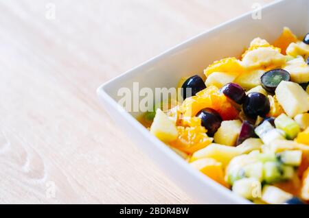 Ein Obstsalat in einer weißen Schüssel auf einem Holztisch Stockfoto
