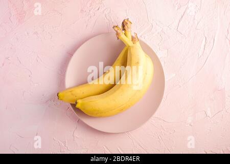 Bananenfrüchte in rosa Platte auf rosa strukturierten Hintergrund, Ansicht von oben Kopierraum Stockfoto