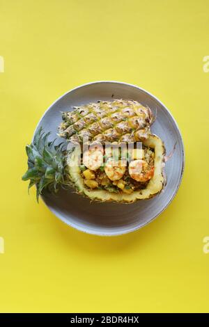 Vogelperspektive Ananas gebratener Reis mit Garnelen in Ananas auf weißem Teller mit gelber Kulisse, umweltfreundlicher Futterbehälter Stockfoto