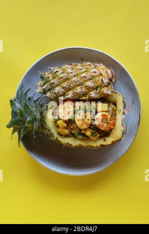 Vogelperspektive Ananas gebratener Reis mit Garnelen in Ananas auf weißem Teller mit gelber Kulisse, umweltfreundlicher Futterbehälter Stockfoto