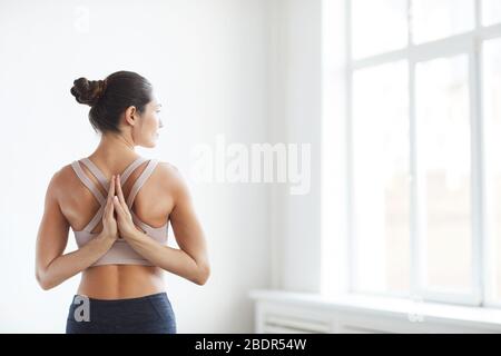 Rückansicht der jungen gesunden Frau, die ihre Hände hinter dem Rücken versteckt und während des Yoga in der Klasse meditiert Stockfoto