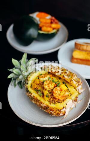 Ananas gebratener Reis mit Garnelen in Ananas auf weißem Teller mit gelber Kulisse, umweltfreundlicher Lebensmittelbehälter Stockfoto