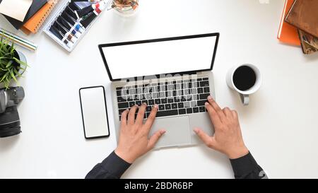 Draufsicht Kreative Hände des Mannes Eingabe auf Computer-Laptop mit weißen leeren Bildschirm, dass setzen auf weißen Arbeitstisch mit Kaffeetasse umgeben, leer Stockfoto