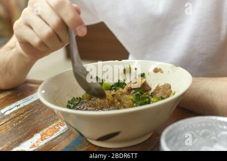 Mann in weißem T-Shirt essen Reisnudelsuppe mit Fleischbällchen Stockfoto