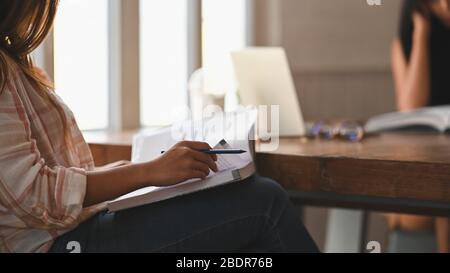 Zugeschnittenes Bild von jungen schönen Frauen Nachhilfe / Lesen eines Buches während sitzen zusammen am Holztisch über Vintage-Wohnzimmer als Hintergrund. Stockfoto