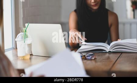 Zugeschnittenes Bild von jungen schönen Frauen Nachhilfe / Lesen eines Buches während sitzen zusammen am Holztisch über Vintage-Wohnzimmer als Hintergrund. Stockfoto