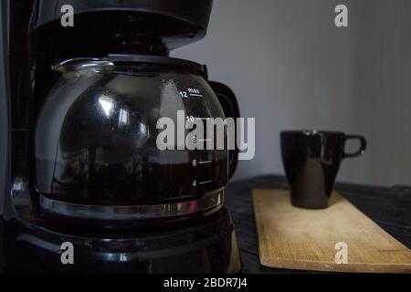 Elektrische Kaffeekanne, schwarze Tasse auf Holztisch, alle auf schwarzem Holz und grauem Hintergrund platziert. Stockfoto