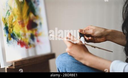 Beschnittenes Bild von schönen Frau Künstler Hände beim Mischen Farbe auf der Holzfarbpalette während vor dem Gemälde Leinwand mit modernen sitzen Stockfoto