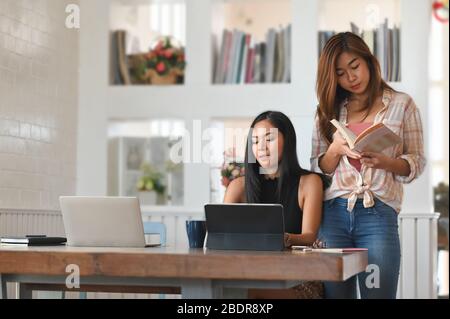 Foto von zwei schönen Frau während der Nachhilfe eine Unterrichtsstunde von der Universität an der modernen Holztisch mit Computer-Tablet, Laptop und Bücher mit comf Stockfoto