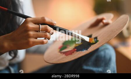Zugeschnittenes Bild von der Hand der Künstlerin Frau, die eine Ölfarbe auf Leinwand mit Pinsel im modernen Kunststudio zeichnet. Konzept junger Künstler/Maler. Stockfoto