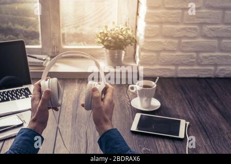 Der Mann, der Musik hört und Kopfhörer hält, erholt sich zu Hause und hat eine Tasse Tee aus der Sicht Stockfoto