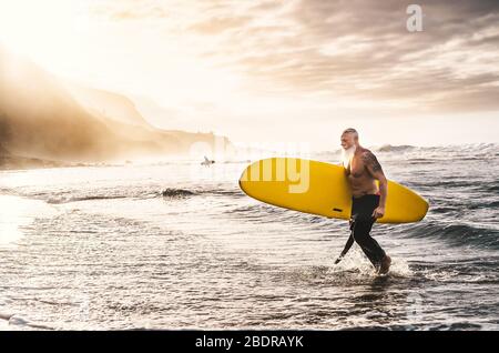 Happy Fit Senior Surfen am Sonnenuntergang Zeit - Sportlich reifen Mann mit Spaß Training mit Surfbrett im Meer Stockfoto