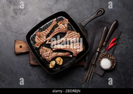 Gegrillte Lammrippen in Bratpfanne. Heißes Lammregal mit Gewürzen und Gewürzen. Draufsicht auf Steintisch Stockfoto