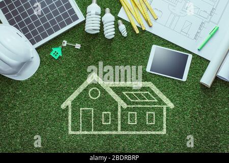 Nachhaltige Hausprojekte und grünes Gebäudekonzept: Blaupause, Solarpanel und Werkzeuge auf üppigem Gras Stockfoto