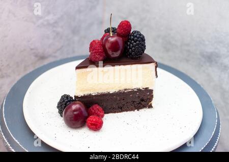 Ein Stück Kuchen in Scheiben geschnitten. Schokoladenbrownie-Teig und Vanillekäsekuchen auf der Oberseite. Dekoriert mit frischen Beeren und geschmolzener Schokolade. Stockfoto