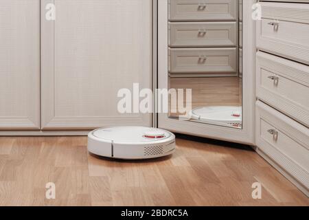 Reflektion von weißen Roboter-Staubsauger läuft vor dem Spiegel im Schlafzimmer. Moderne intelligente Gerät für die Reinigung Haus. Stockfoto