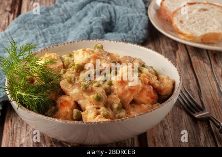 Hähnchenfilet mit grünen Erbsen, die in einer cremigen Soße auf einem Holztisch gedünstet sind Stockfoto