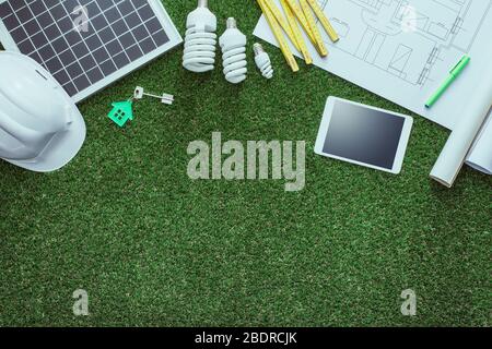 Nachhaltige Hausprojekte und grünes Gebäudekonzept: Blaupause, Solarpanel und Werkzeuge auf üppigem Gras Stockfoto