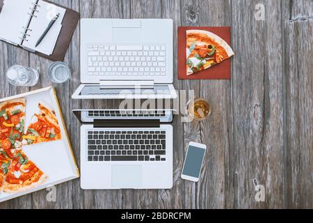 Büroschreibtisch mit Laptop und Pizza in einer Schachtel, Mittagspause Stockfoto
