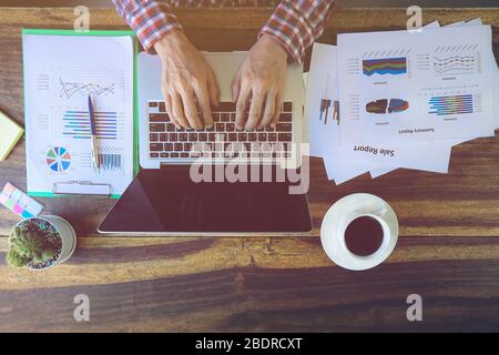 Geschäftsmann analysiert Anlagekarten auf Papier und mit Laptop im Büro Stockfoto