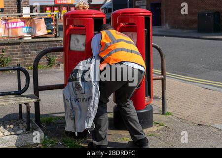Ein Postbote der Royal Mail, der eine Brieftasche trägt, die Post aus einem Briefkasten auf einer Straße sammelt Stockfoto