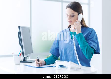 Junge Ärztin und Praktiker, die Arbeiten an der Rezeption, sie ist beantwortet Anrufe und Terminvereinbarungen Stockfoto