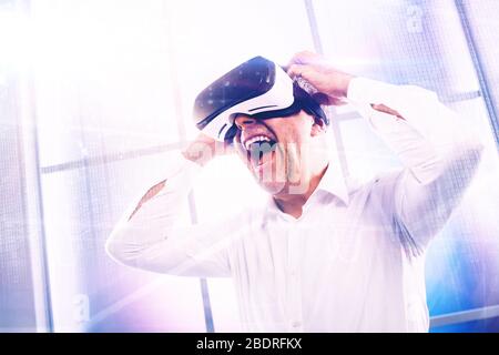 Fröhlicher, reifer Mann, der ein VR-Headset trägt und mit einer virtuellen Realitätsumgebung interagiert Stockfoto