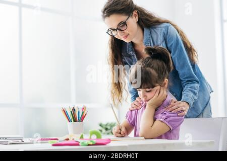 Mutter und Kind gemeinsam Hausaufgaben zu machen zu Hause, die Frau steht hinter das Mädchen und hilft ihr, Stockfoto