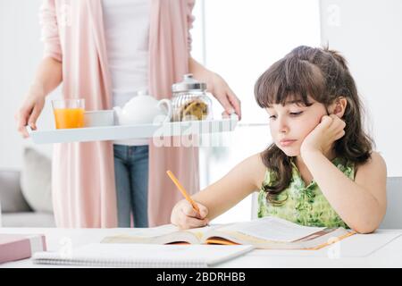 Süße Mädchen studieren zu Hause, ihre Mutter bringt ihr einige gesunde Snacks, Familie und Lifestyle Konzept Stockfoto