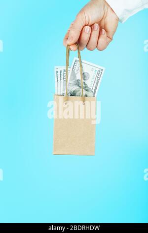 Eine kleine Papiertüte in der Hand mit US-Dollar auf blauem Hintergrund. Layout der Verpackungsvorlage mit Platz zum Kopieren, Werbung. Stockfoto