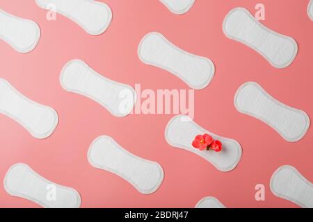 Sanitäre Pads auf pinkfarbenem Hintergrund in Form eines diagonalen Wiederholungspusters, mit einer roten Blume auf dem Pad. Stockfoto