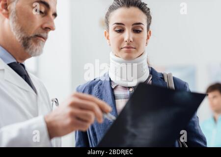 Arzt bei der Untersuchung des Röntgenstrahls einer jungen Patientin trägt sie einen Halsschild und hat eine schwere Wirbelsäulenverletzung Stockfoto