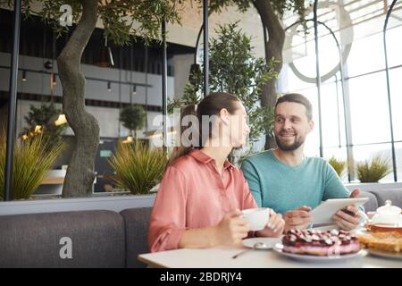 Junges Paar mit Tablet-pc und miteinander reden, während am Tisch im Café sitzen Stockfoto