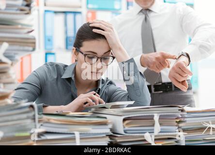 Anspruchsvolle boss verweist auf seine Uhr und bittet, seine Mitarbeiter, sich zu beeilen, seine Sekretärin ist frustriert und mit Arbeit überhäuft: deadlin Stockfoto