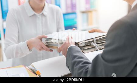 Der Chef übergibt seinem jungen weiblichen Angestellten Papiere Stockfoto