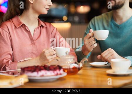 Nahaufnahme eines jungen Paares, das am Tisch sitzt, Tee mit Kuchen trinkt und sich miteinander unterhält Stockfoto