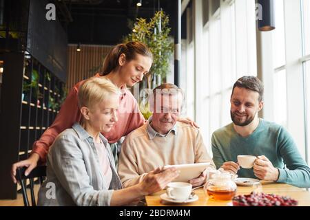 Vierköpfige Familie führt Online-Gespräche mit ihren Verwandten auf einem digitalen Tablet, während sie im Restaurant zu Mittag essen Stockfoto