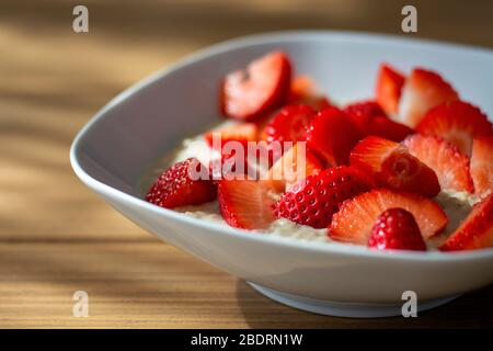 Hausgemachte Haferbrei Haferbrei Schüssel mit Erdbeeren in Scheiben geschnitten auf Holztisch in der Morgensonne. Gesunde Mahlzeit. Haferbrei Stockfoto