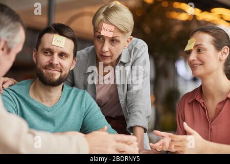 Vierköpfige Familie sitzt am Tisch und hat Spaß zusammen spielen sie das Spiel mit Aufklebern auf der Stirn Stockfoto