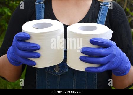 Die letzten beiden Rollen Toilettenpapier in den Händen einer Dame, die medizinische Handschuhe trägt. Stockfoto
