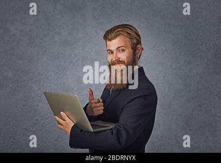 Portrait gut lächelnd Geschäftsmann Arbeit mit Laptop geben Daumen nach oben isoliert grauen Hintergrund Wand Stockfoto
