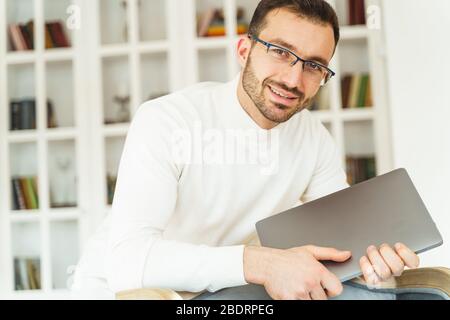 Lächelnder junger Büroangestellter, der einen Laptop hält Stockfoto