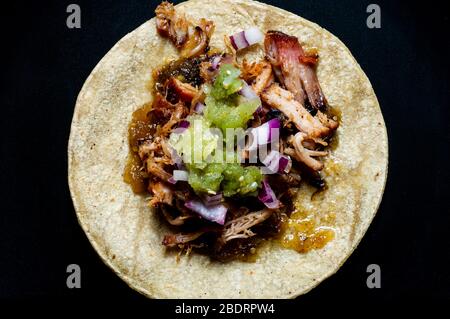 Carnitas Tacos mit roten Zwiebeln und roher Salsa verde. Mexikanische langsam gekochte Schweinefleisch Gericht auf schwarzem Teller isoliert Stockfoto