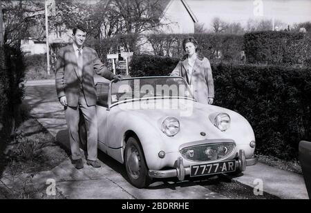1960er Jahre, historisch, ein junges erwachsenes Paar, das neben ihrem offenen Sportwagen Austin-Healey Sprite stand, parkte neben einer Hecke auf einer schmalen Betonzufahrt im Eastholm Green in Letchworth Garden City, England, Großbritannien. Der kleine Zweisitzer Sprite, der als Nachfolger des Vorkriegs Austin Seven entworfen wurde, wurde zwischen 1958-1961 in Großbritannien produziert und mit seinen Scheinwerfern, die aus der Fronthaube kommen, wurde er liebevoll als "Frogeye" bekannt. Stockfoto