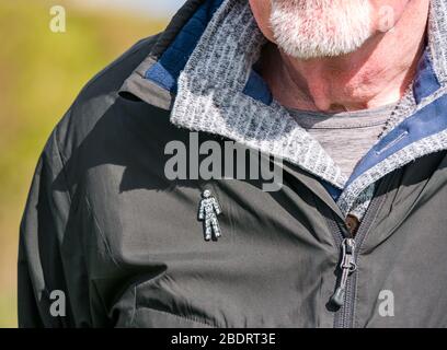 Älterer Mann mit grauem Bart, der den Prostate Cancer UK Charity Badge Pin trägt, der an der Jacke befestigt ist, um das Bewusstsein für die allgemeine Gesundheit zu schärfen, Großbritannien Stockfoto
