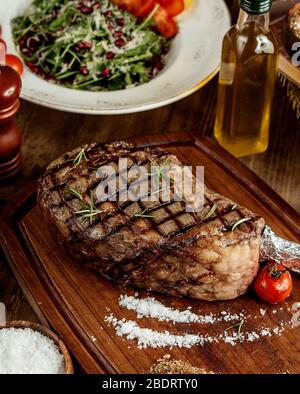 Gegrilltes Steak mit Salzkräutern und gegrillter Tomate auf Holzbrett serviert Stockfoto
