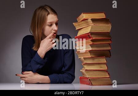 Junge Mädchen und viele Bücher neben ihr, sie hat schwer zu lernen Stockfoto